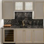 Gray kitchen with gold-trimmed cabinets, black marble backsplash and solid-surface countertop, gold faucet over a sink.