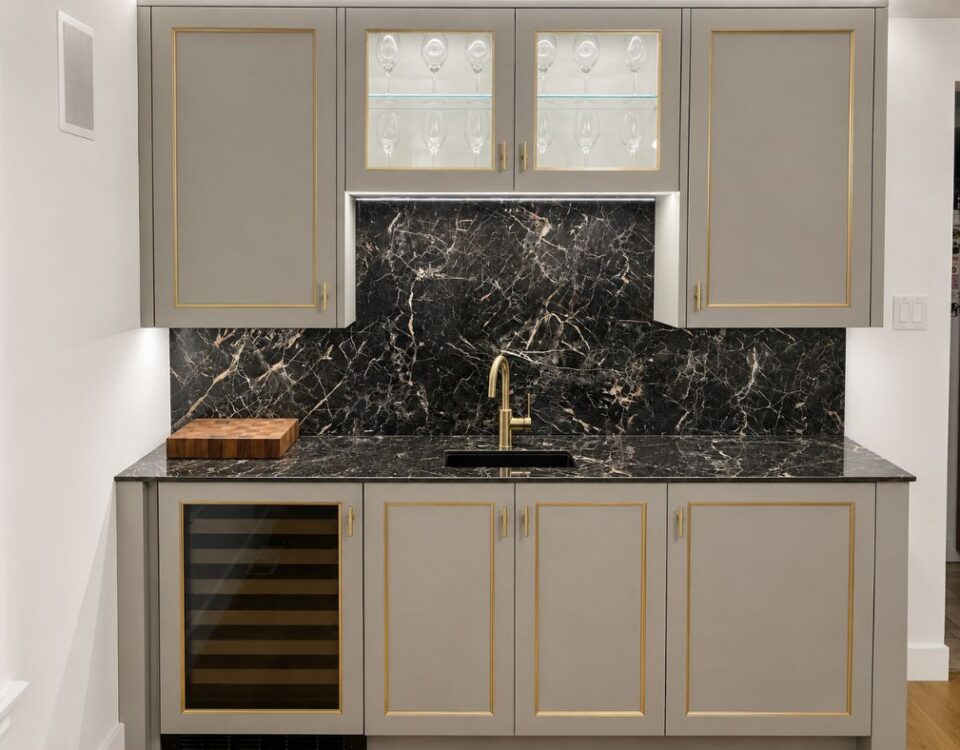 Gray kitchen with gold-trimmed cabinets, black marble backsplash and solid-surface countertop, gold faucet over a sink.